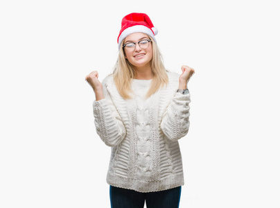 年轻的高加索女人戴着圣诞帽，在孤立的背景上庆祝，惊讶和惊讶的成功，举起手臂和睁开眼睛。 赢家概念。