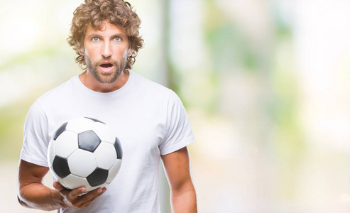 一个英俊的西班牙裔男子男子在孤立的背景下捧着足球，吓得满脸惊讶恐惧和兴奋