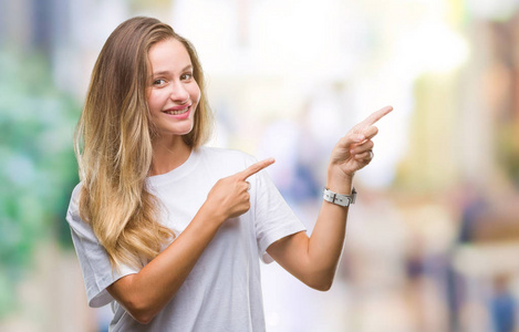 年轻漂亮的金发女人穿着休闲的白色T恤，在孤立的背景上微笑着，用两只手和手指对着镜头。