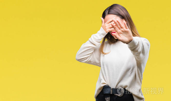 年轻漂亮的女人休闲白色毛衣,在孤立的背景上,用手遮住眼睛,用悲伤和
