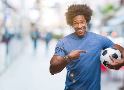 美国黑人男子抱着足球在孤立的背景下非常高兴地用手和手指指点