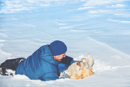 一个快乐的人，冬天躺在雪地上，养着一只拉布拉多猎犬。 狗躺在背上