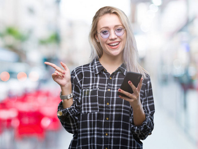 年轻的金发女人用智能手机在孤立的背景下发送信息，非常高兴地用手和手指指向一边。