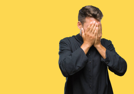 年轻的天主教基督教牧师男子在孤立的背景上,悲伤的表情覆盖着脸,同时