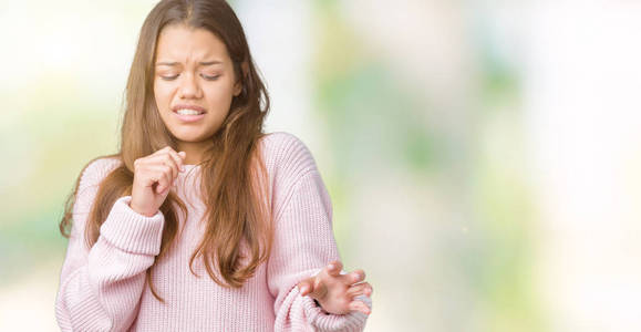 年轻漂亮的黑发女人穿着粉红色的冬季毛衣，在孤立的背景下，厌恶的表情，不高兴和恐惧的做厌恶的脸，因为厌恶的反应。 举起双手。 令人