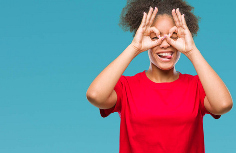 美国妇女在孤立的背景下做好手势,就像望远镜伸出舌头,透过手指看眼睛