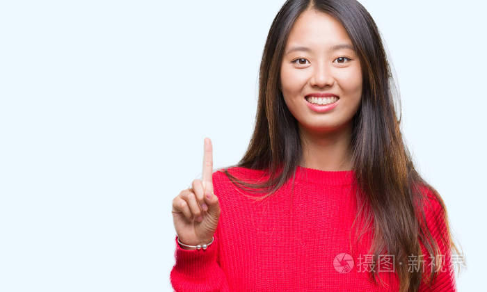 年轻的亚洲女人穿着冬天的毛衣，在孤立的背景上显示和指着第一个手指，同时微笑自信和快乐。