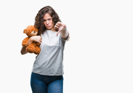 年轻的黑发女孩抱着泰迪熊在孤立的背景和愤怒的脸消极的迹象显示不喜欢拇指向下拒绝概念