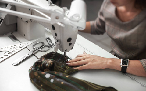 电动缝纫机上女裁缝手缝制服装的细节照片