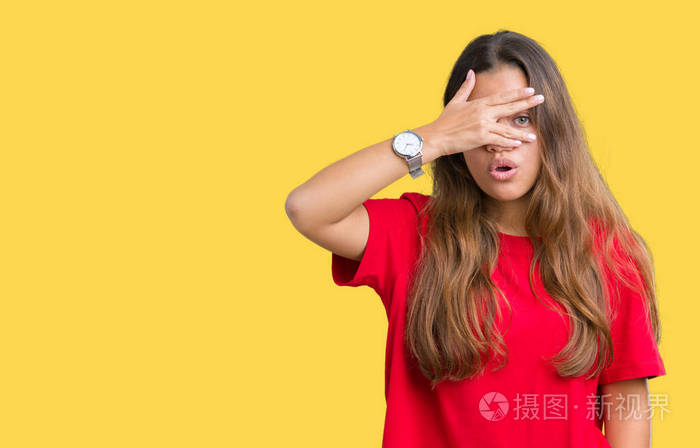 漂亮的黑发女人,穿着红色t恤,在孤立的背景上偷看,震惊地遮住脸和眼睛