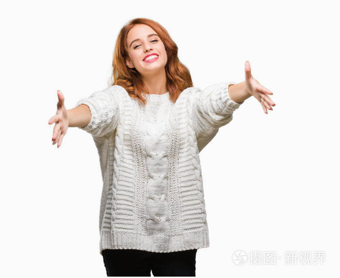 年轻漂亮的女人在孤立的背景上穿着冬天的毛衣,看着相机,张开双臂拥抱