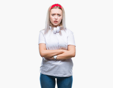 年轻的金发女人戴着耳机听音乐，而不是孤立的背景怀疑，紧张的不赞成表情在脸上交叉的手臂。 消极的人。