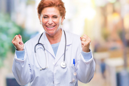 高级白种人医生女士穿着医疗制服，在孤立的背景下庆祝惊讶和惊讶的成功，举起手臂和睁开眼睛。 赢家概念。