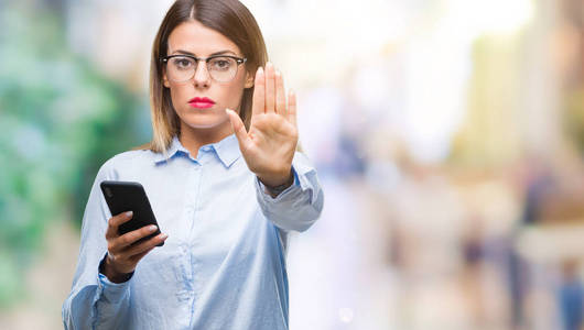 年轻漂亮的商务女性用智能手机在孤立的背景上发短信，张开手做停止标志，严肃自信的表情防御手势