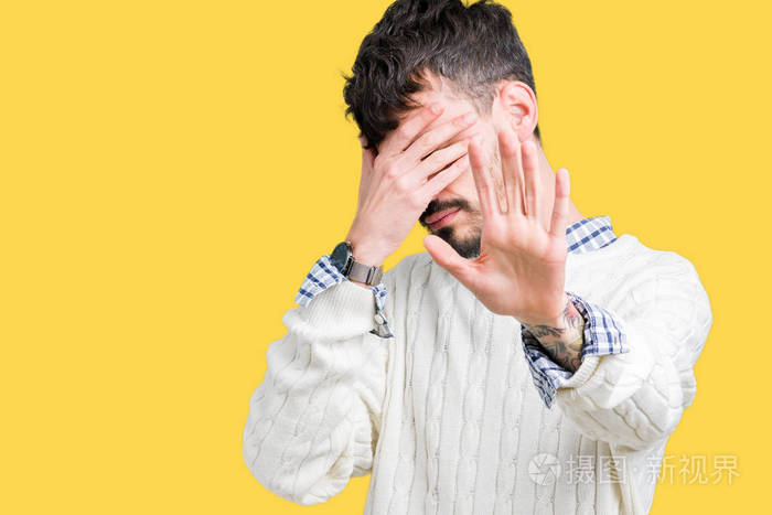 年轻的帅哥穿着冬天的毛衣在孤立的背景上用手遮住眼睛用悲伤和恐惧的