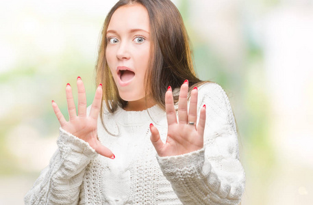 年轻漂亮的白种人女人穿着冬天的毛衣,在孤立的背景下害怕和恐惧,表情
