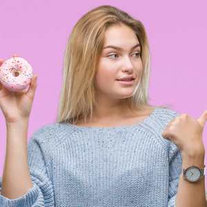 年轻的白种人女人一边吃甜面圈，一边在孤立的背景下指着，一边用拇指露出快乐的脸