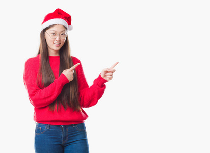 年轻的中国妇女戴着圣诞帽，微笑着看着镜头，两只手和手指指向一边。