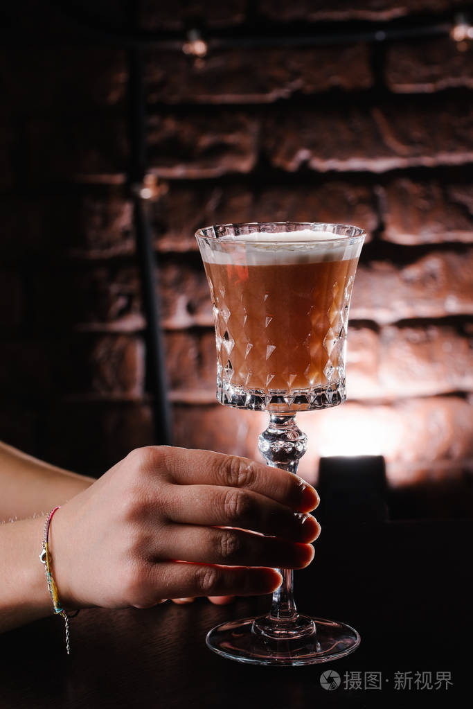 在砖墙背景上拿着鸡尾酒的女人