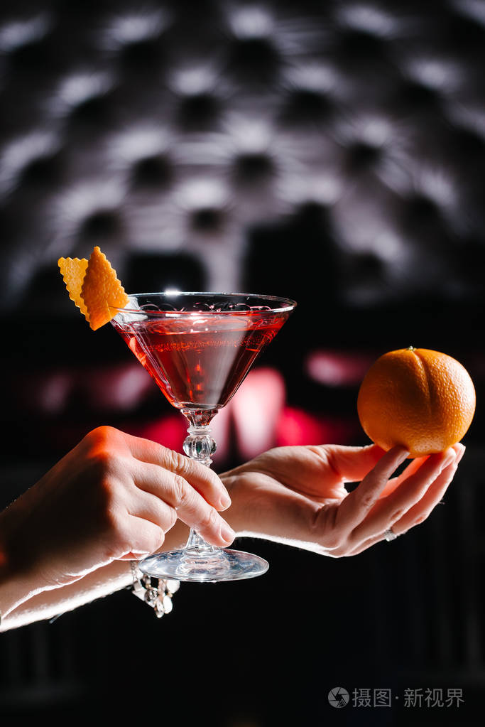 拿着鸡尾酒和橘子的女人拍的