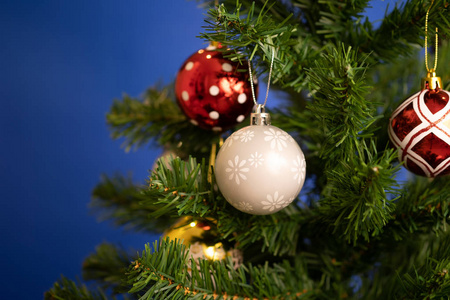 关闭圣诞球装饰品挂在圣诞树和蓝色背景上。