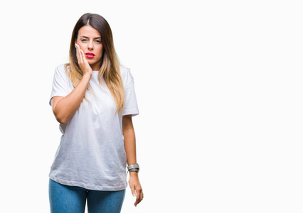 年轻的美女，休闲的白色T恤，在孤立的背景上，用手触摸嘴，因为牙痛或牙齿疾病，表情痛苦。 牙医的概念。
