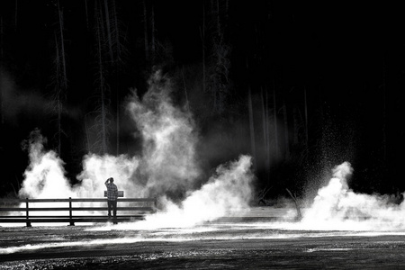 一个人独自站在木板路上，看着水蒸汽，中途喷泉盆地黄石国家公园