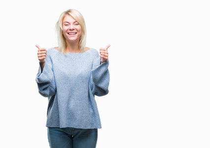 年轻漂亮的金发女人穿着冬天的毛衣，在孤立的背景上，成功的标志，用手竖起大拇指，微笑和快乐地做积极的手势。 用欢快的表情看着相机，