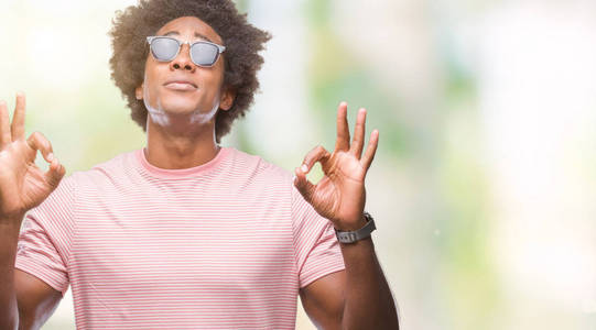 美国黑人男子戴着太阳镜在孤立的背景上放松和微笑，闭着眼睛做冥想手势用手指。 瑜伽概念。