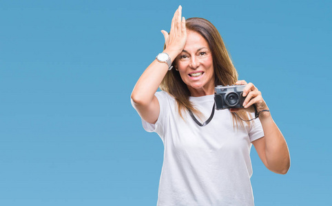 中年西班牙裔妇女拍照使用老式照片相机在孤立的背景上强调，手在头上震惊，羞愧和惊讶的脸，愤怒和沮丧。 因为错误而恐惧和不安。