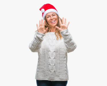 中年老年西班牙裔妇女戴着圣诞帽，在孤立的背景上展示和举着十个手指，同时微笑着自信和快乐。