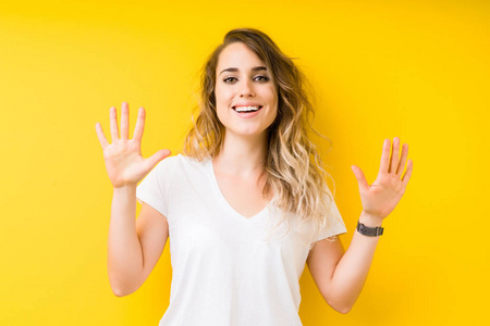 年轻漂亮的金发女人在黄色的背景下，用十号手指，微笑着自信和快乐。