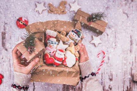 木制背景上的圣诞礼物姜饼。 节日包装中的饼干。 女人手拿着圣诞礼品盒，把圣诞姜饼饼干包装在盒子里。 上面的风景。 复制空间