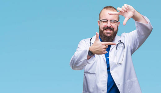 年轻的白种人医生穿着医用白色外套，在孤立的背景上微笑，用手和手指制作框架，用快乐的脸。 创造力和摄影理念。