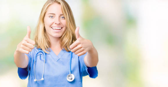 美丽的年轻医生女士穿着医疗制服，在孤立的背景下，批准用手竖起大拇指做积极的手势，微笑，为成功而高兴。 看着相机赢家的手势。
