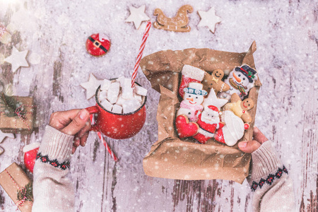 女人的手拿着一个圣诞姜饼饼干在一个盒子和热巧克力与棉花糖。 圣诞礼物可可饮料红色杯子和新年。 手工制作。