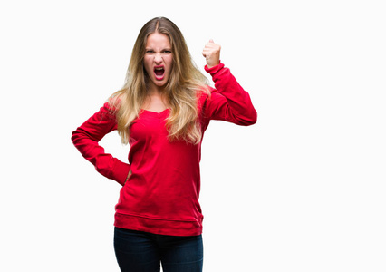 年轻漂亮的金发女人穿着红色毛衣，在孤立的背景下，愤怒和疯狂地举起拳头，沮丧和愤怒，大声喊叫。 愤怒和侵略性的概念。