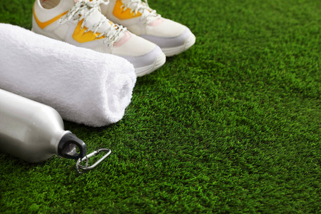 一瓶水运动鞋毛巾和空间的文字在人造草。 健身器材
