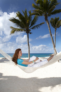 美丽的年轻女子在棕榈树和大海背景下的海滩上的吊床上