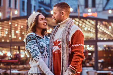 一对年轻的浪漫夫妻在圣诞节的时候站在大街上, 享受在一起的时光, 手牵手看着对方