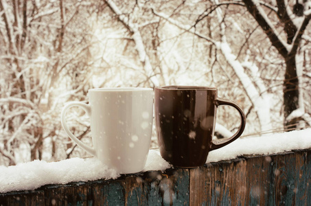 舒适的冬季静物在白雪覆盖的露台上喝两杯热咖啡或茶。 森林里寒冷的冬日。 圣诞节假期。 冬天舒适的背景
