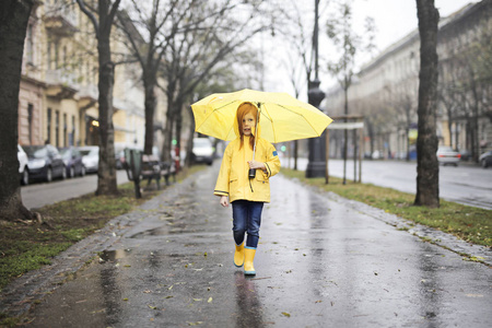 穿着雨衣和雨伞走在街上的小女孩