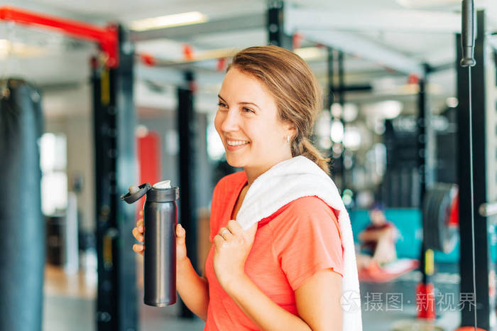 运动健身房里快乐而疲惫的女人拿着白色毛巾和一瓶水