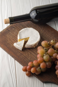 白色木制背景上的葡萄酒瓶，有葡萄和卡蒙伯特奶酪