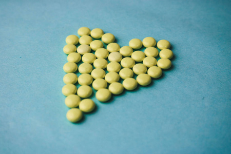 小药用圆形黄色药丸, 维生素, 药物, 抗生素的形式心脏上的蓝色背景