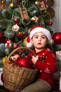 一个戴着圣诞帽的小男孩正在用红色玩具装饰一棵圣诞树。 为圣诞节和新年做准备。