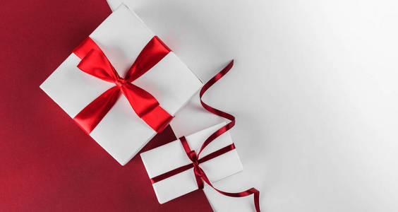 圣诞礼品盒与红色丝带装饰杉树枝松果在白色和红色纸背景。 圣诞节和新年快乐主题。 平躺顶部视图空间文本