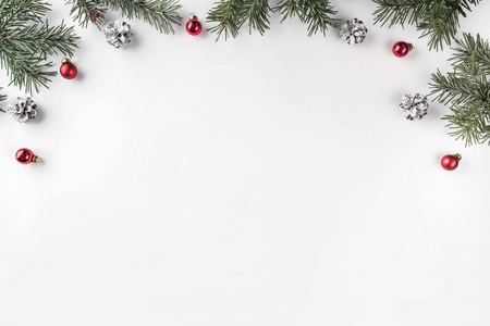 创意框架由圣诞杉木树枝在白色背景与红色装饰松果。 圣诞节和新年主题。 平躺式顶部视图