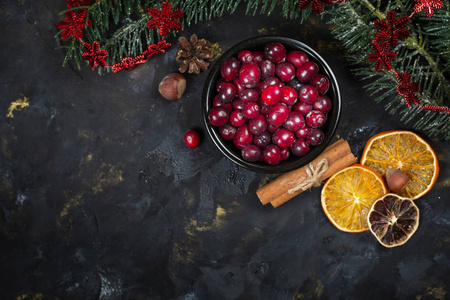 带有圣诞树树枝干橙肉桂棒和一碗新鲜蔓越莓的深色背景，俯视