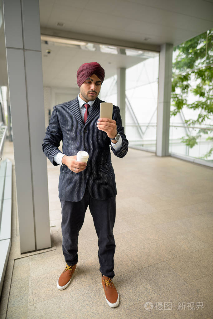 印度商人在城市拿着咖啡杯和手机